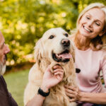 A senior couple enjoys a warm moment with their golden retriever in a lush green park.